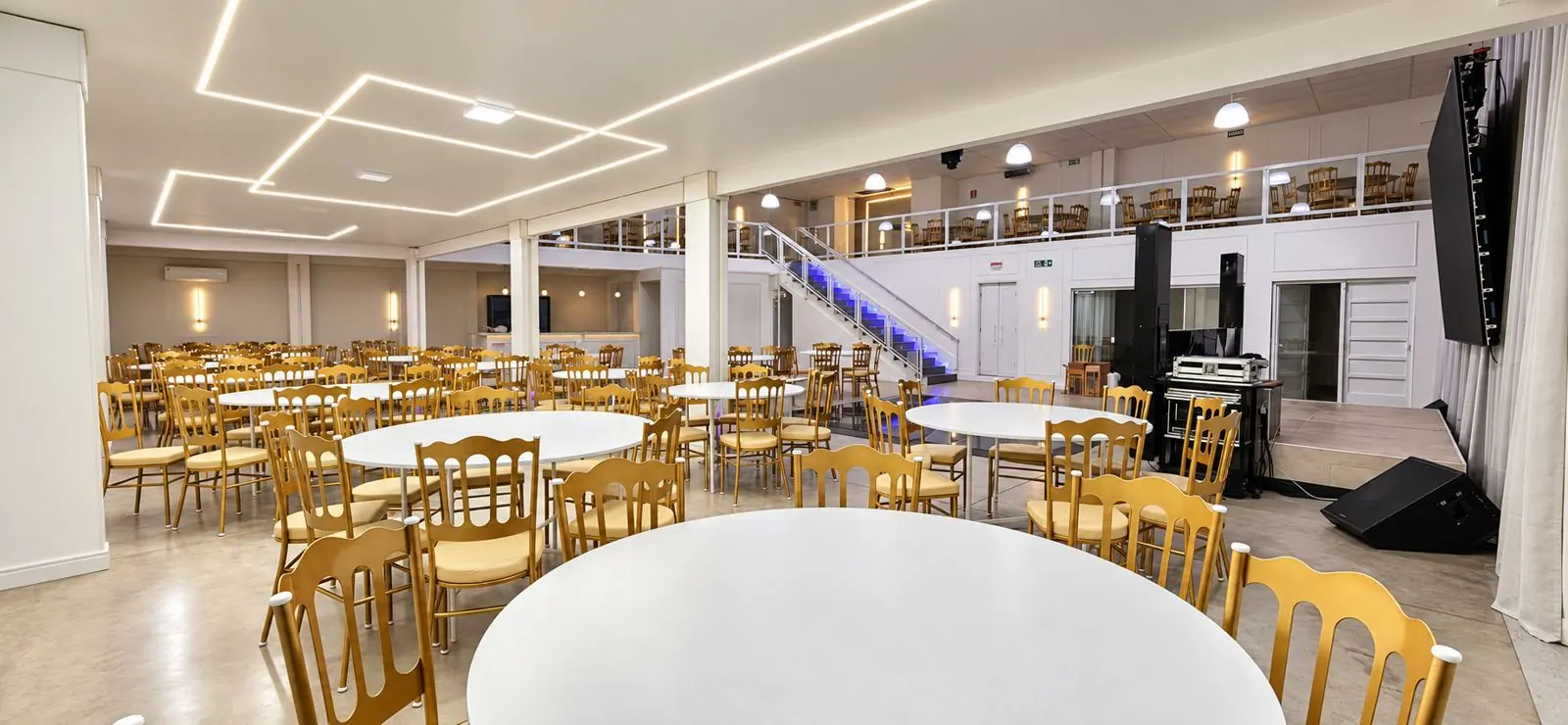 Salão principal com mesas redondas, cadeiras douradas e palco